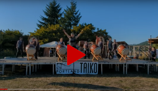 A screenshot from YouTube with a red Play button arrow and a taiko group in the background
